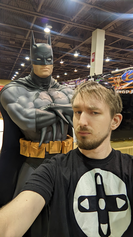 Alex looking dramatically at the camera, while wearing a Game Direction company logo. A Batman statue is over his shoulder.