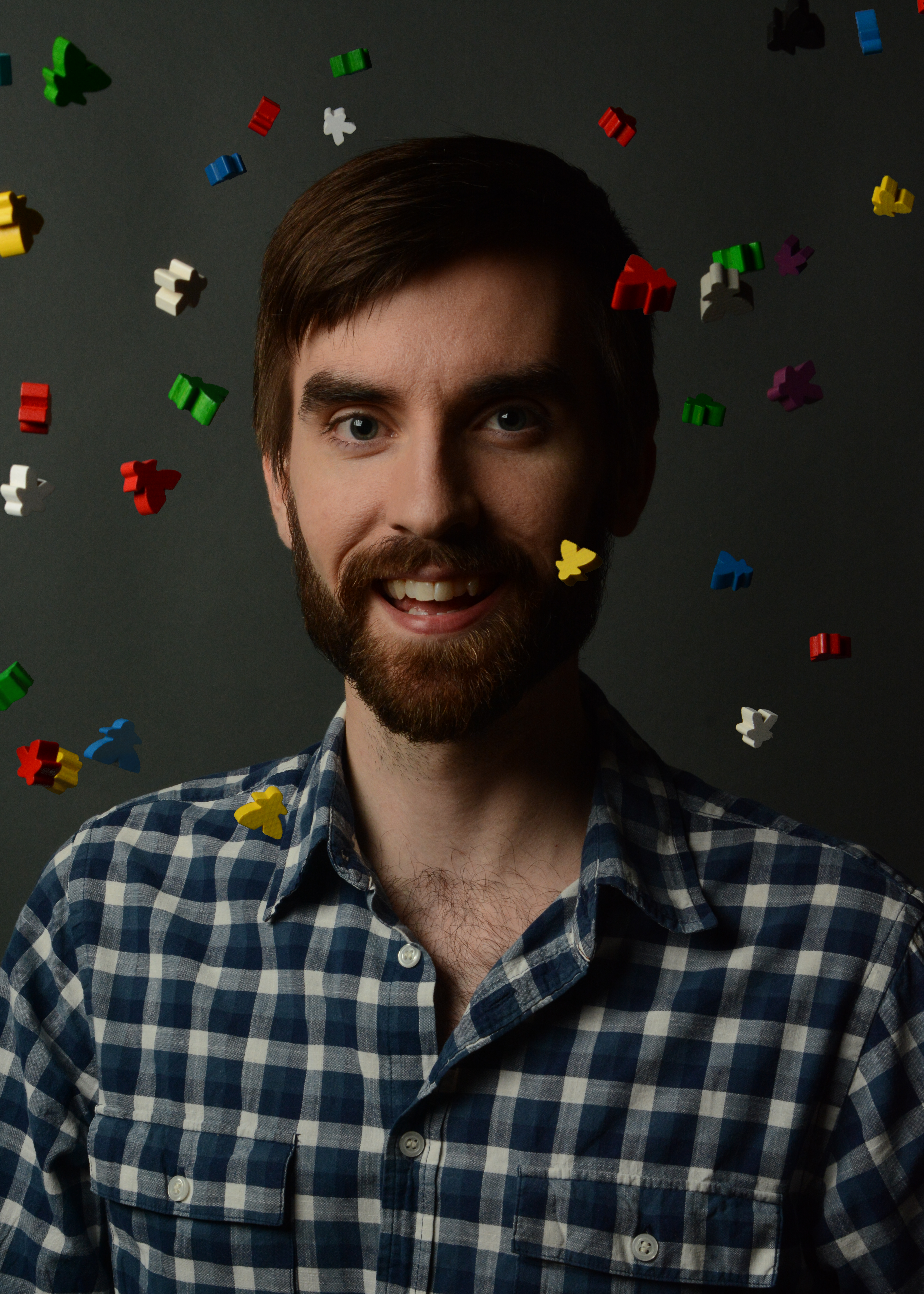 Dsvid Van Drunen smiling brightly into the camera, his checked shirt opened casually at the collar, while multi-coloured meeples rain down around him