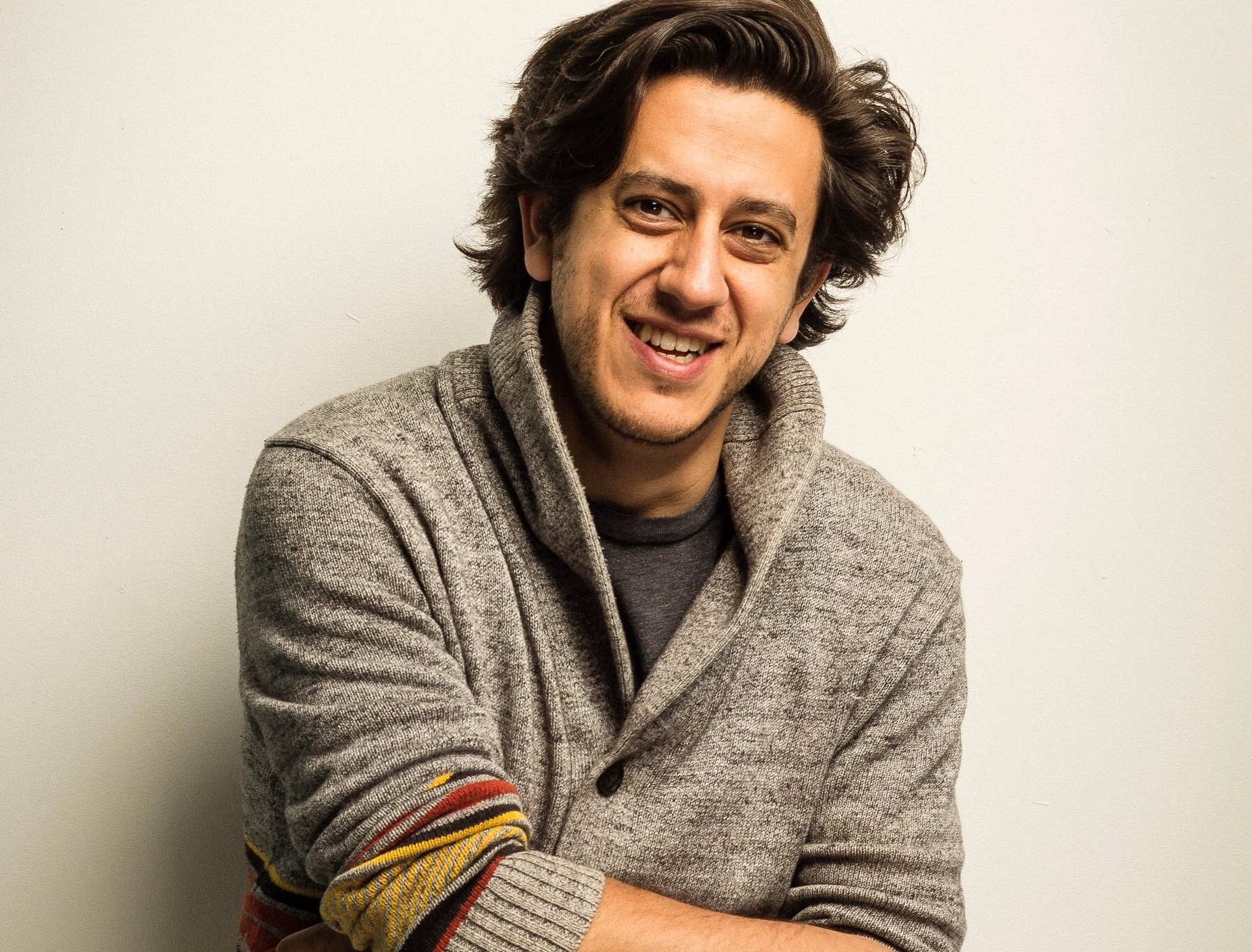 Kris Siddiqi wearing a finely knit sweater, smiling effortlessly at the camera