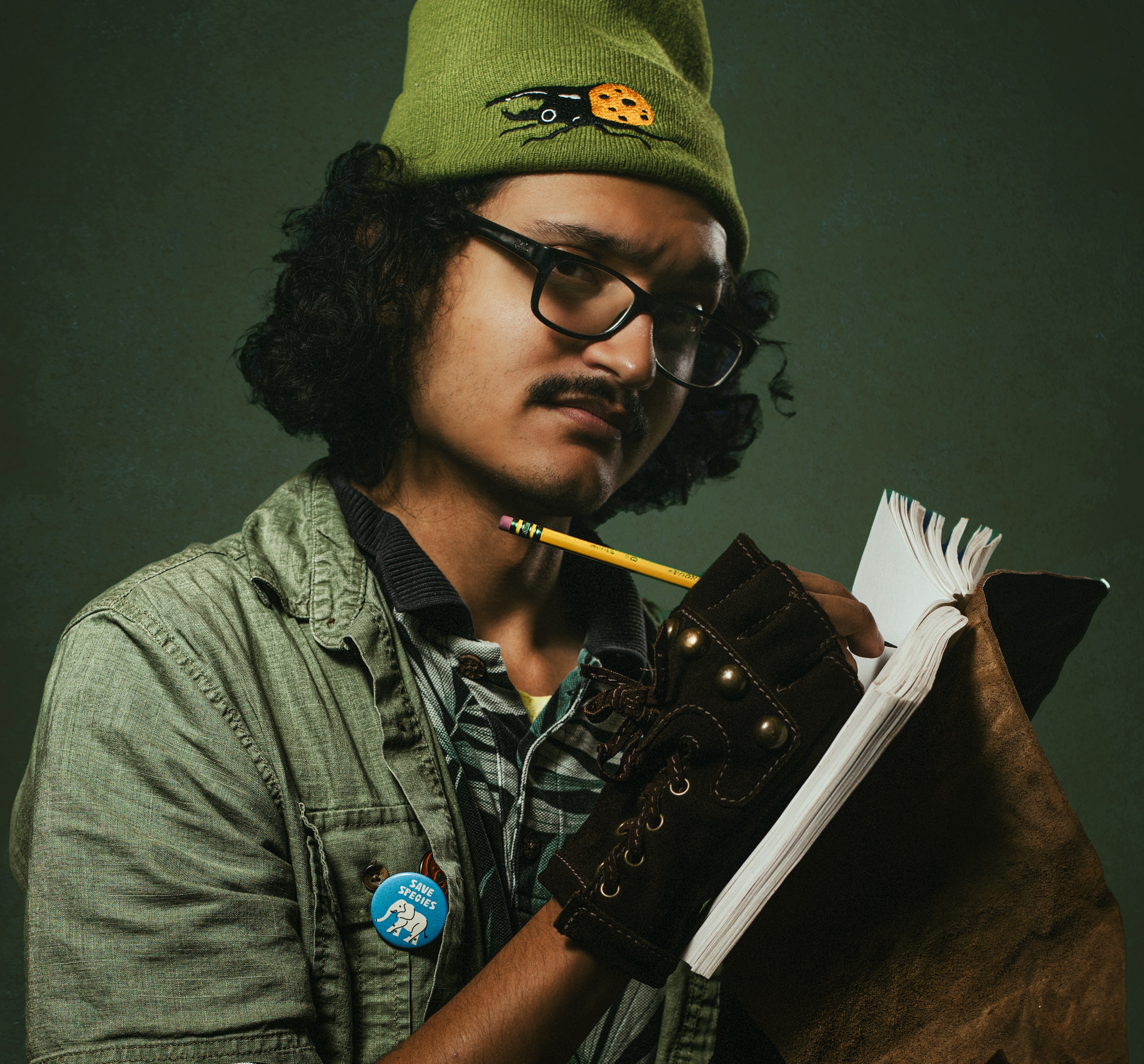 Andrew Rivera, wearing a green toque with a beetle on it, writes in a leather bound notebook