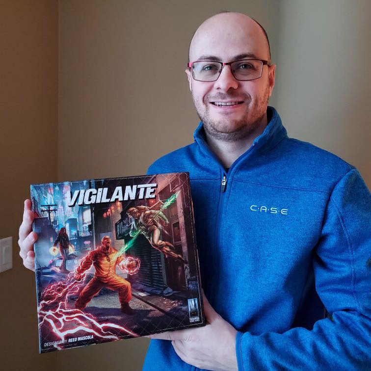 Reed in a blue hoodie holding a copy of his game vigilante