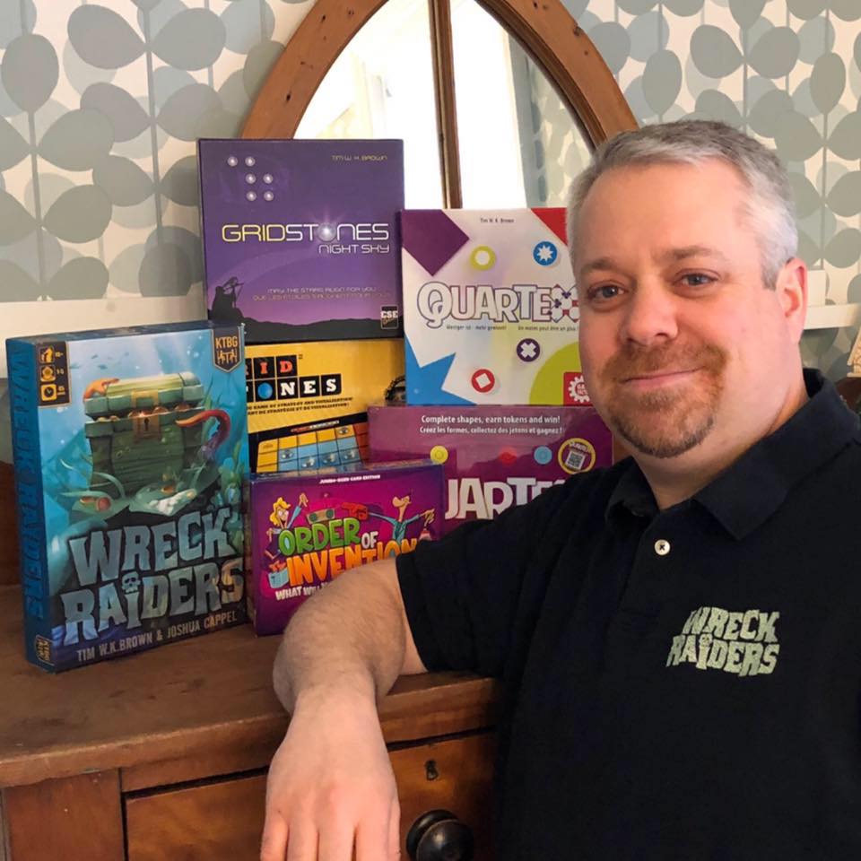 Tim W. K. Brown is standing in front of his most popular games: Wreck Raiders, Quartex, Gridstones, and Order of Invention.