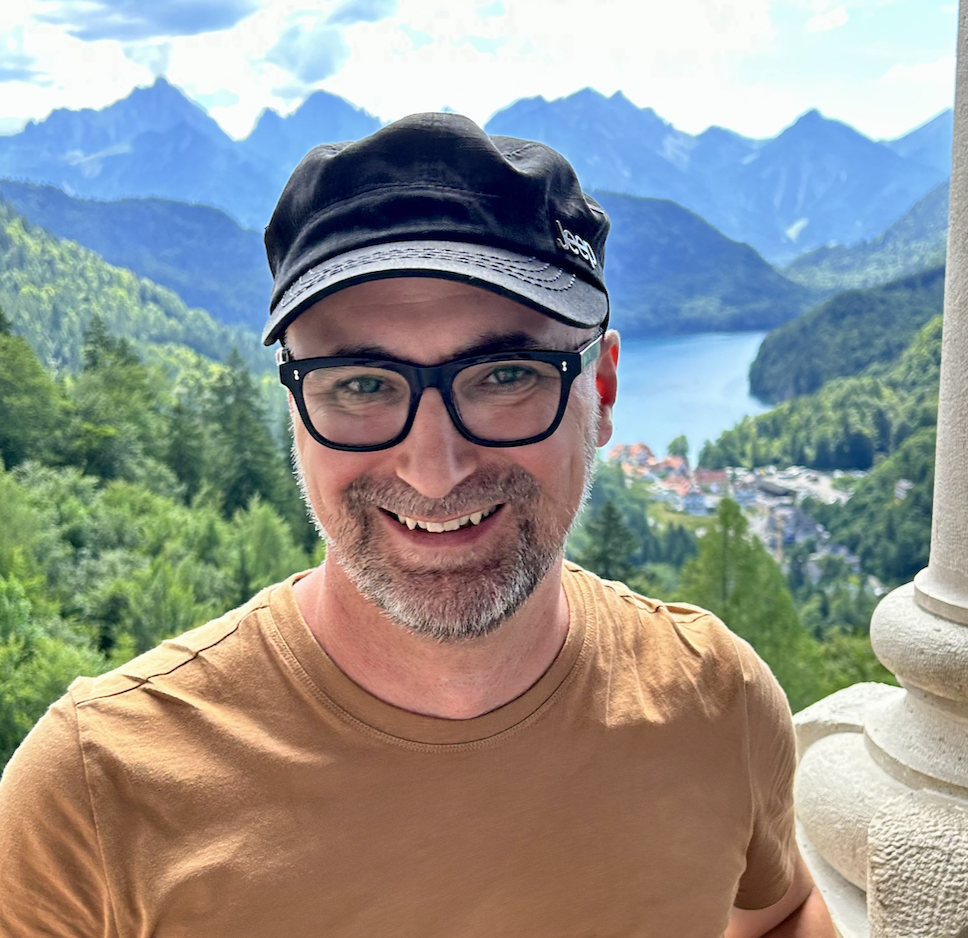 Headshot of Derek Gour with a mountain landscape in the background