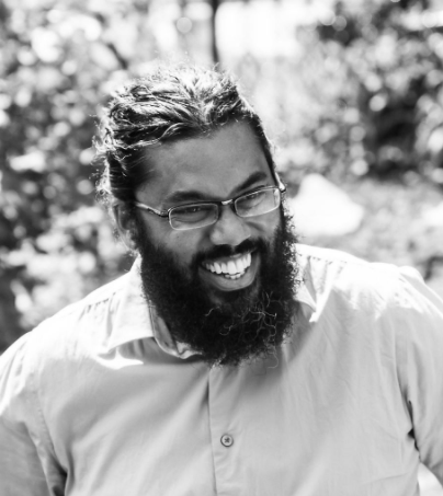 Black and white headshot of Ryan Khan laughing with trees in the background.  