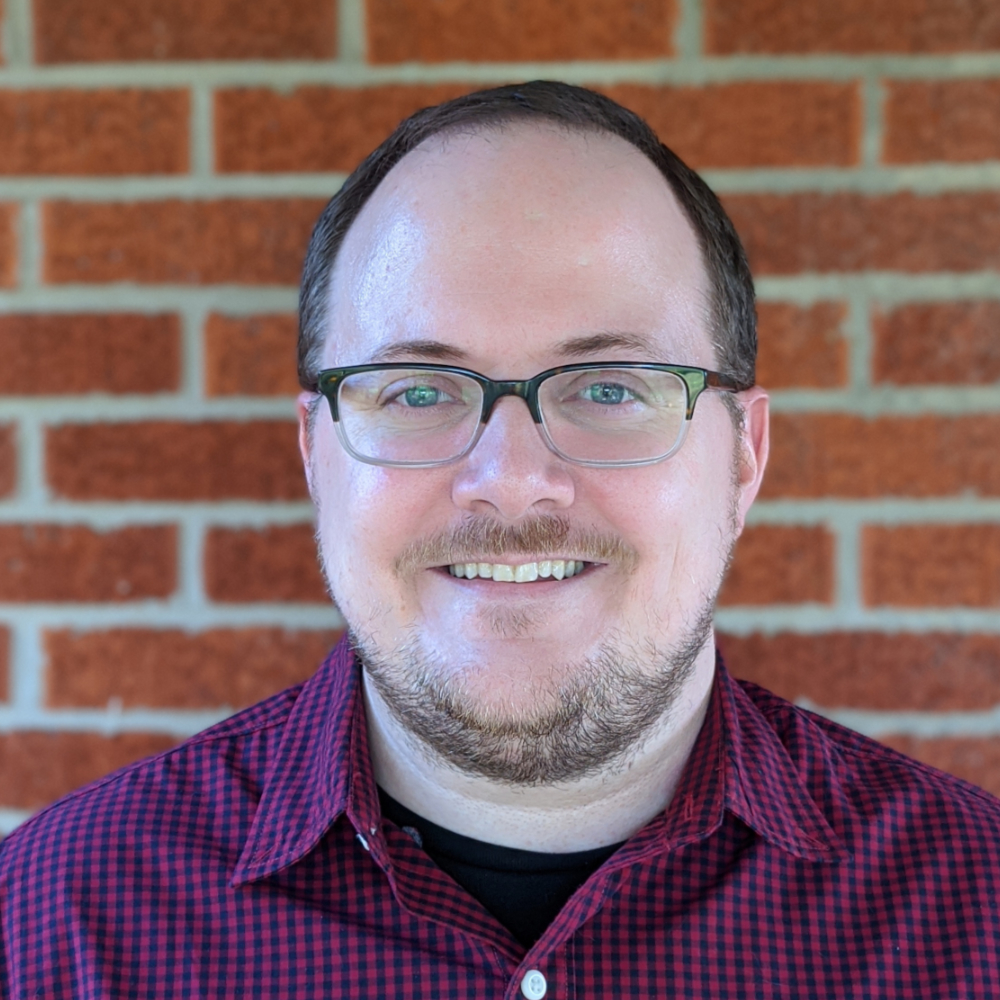 Headshot of Ken Lowery smiling in front of a brick wall. 