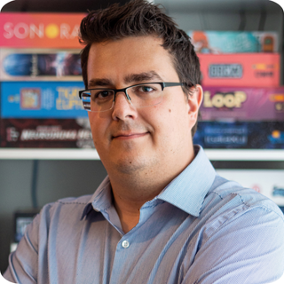 Jeff Fraser standing in front of a book shelf of board games.