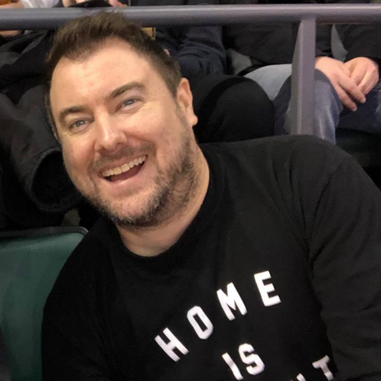 Sean looks to be seated at a sporting event, wearing a shirt that says home is toronto. 