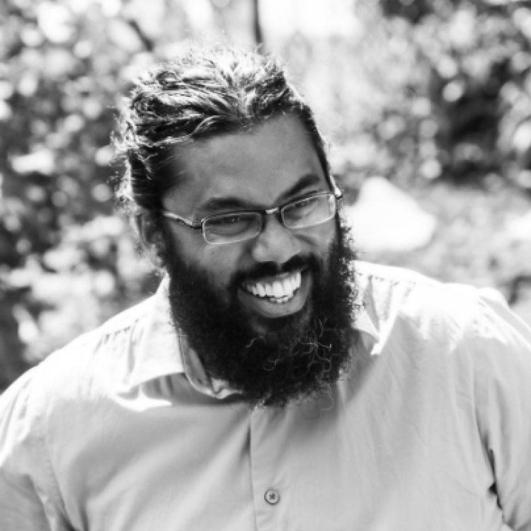 Black and white headshot of Ryan Khan laughing with trees in the background.  