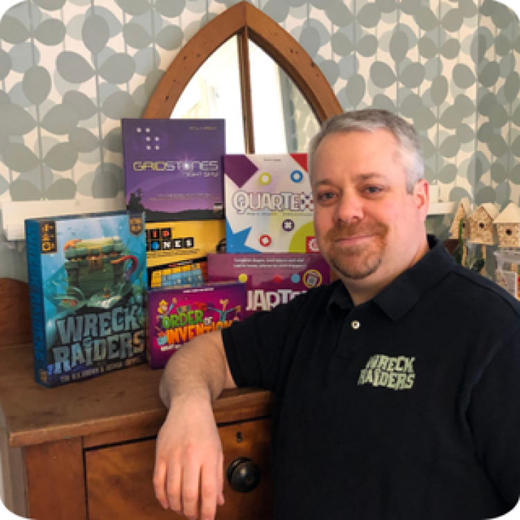 Tim W. K. Brown standing in front of his most popular games: Wreck Raiders, Quartex, Gridstones, and Order of Invention.
